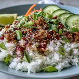 Fluffy rice and sizzling ground turkey are covered in bang bang sauce, with crunchy carrots, cucumbers, cabbage, and lime wedges.