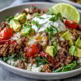A Low Carb Burrito Bowl with seasoned beef, crisp lettuce, avocado, and a drizzle of sour cream.
