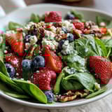 A vibrant Spinach and Berry Salad Bowl garnished with toasted walnuts and red onion, ready for a healthy side dish.