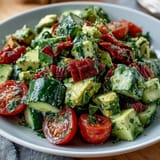 Cucumber Tomato Avocado Salad with Lemon Dressing in a white bowl, vibrant and fresh with colorful vegetables and a glossy lemon dressing.