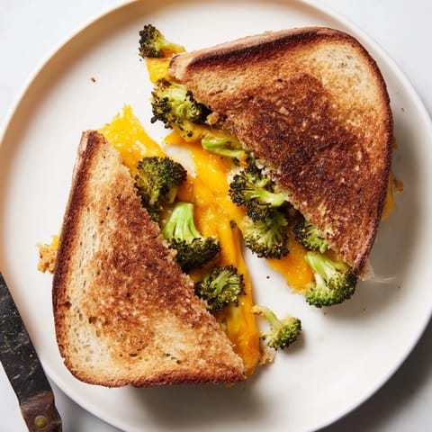 Roasted broccoli & cheddar grilled cheese sandwich oozing gooey cheese, served with tomato soup.