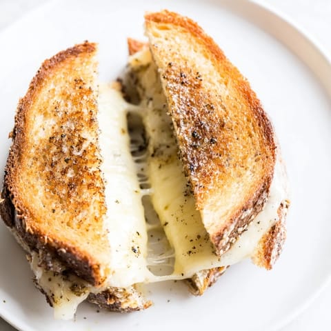 A close-up of a buttery Truffle Grilled Cheese, with gooey Gruyère oozing from the crunchy, golden-brown bread slices.