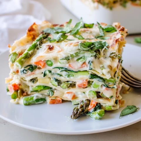 Golden-brown Spring Veggie Alfredo Lasagna fresh from the oven, layered with creamy Alfredo sauce, tender asparagus, peas, and zucchini, garnished with fresh basil on a rustic table.