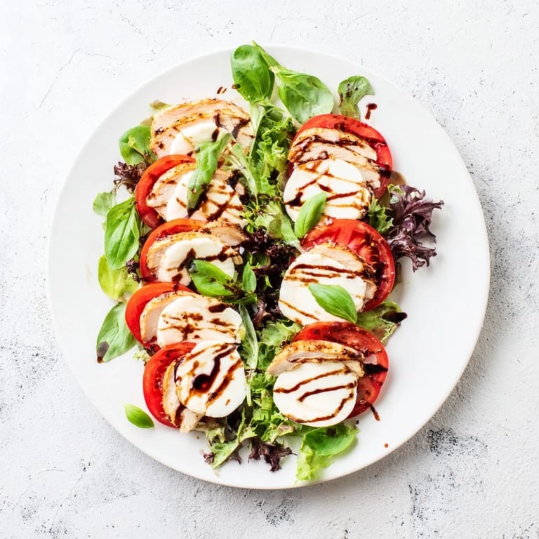 Savory grilled chicken breast nestled among ripe tomato slices, white mozzarella discs, and bright green basil leaves, finished with a glossy balsamic drizzle perfect for a summer lunch.