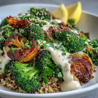 Crispy roasted broccoli florets topped with sesame seeds on fluffy quinoa, drizzled with creamy tahini sauce in a white bowl.