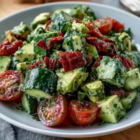 Cucumber Tomato Avocado Salad with Lemon Dressing in a white bowl, vibrant and fresh with colorful vegetables and a glossy lemon dressing.